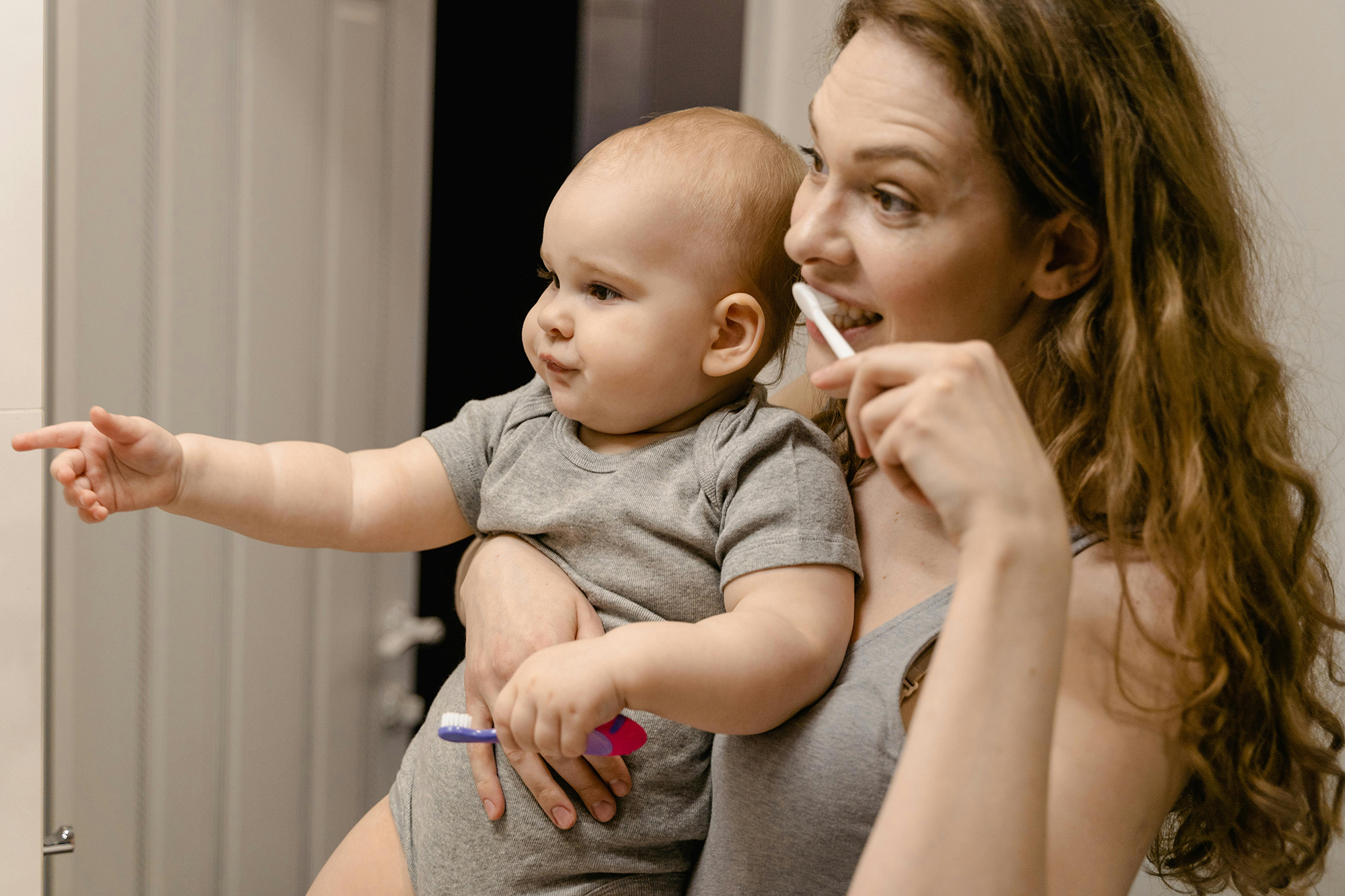 Mom holding baby and brushing her teeth
